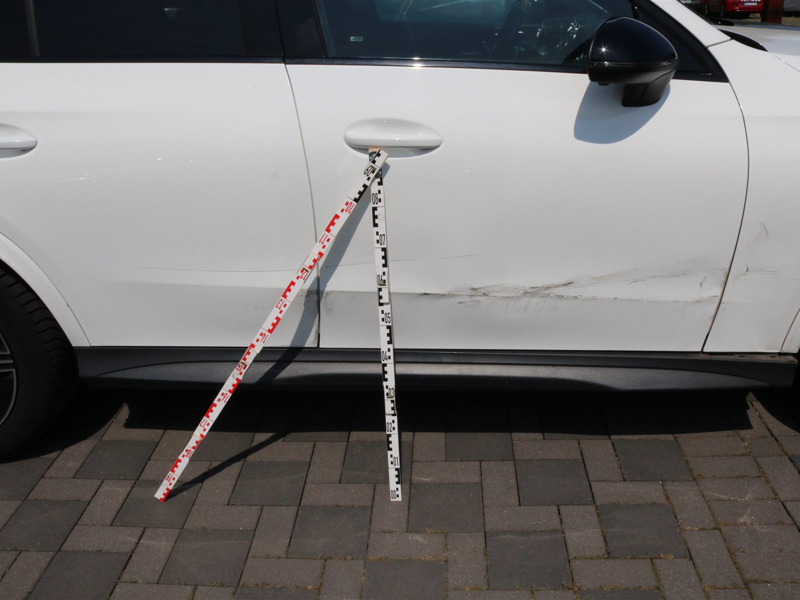 Beschädigte Fahrerseite eines weißen Mercedes GLC Coupé mit Messlatten